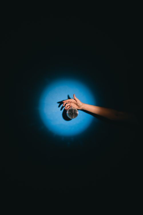 Free A hand elegantly holding a disco ball against a dark background, highlighted by a blue spotlight. Stock Photo