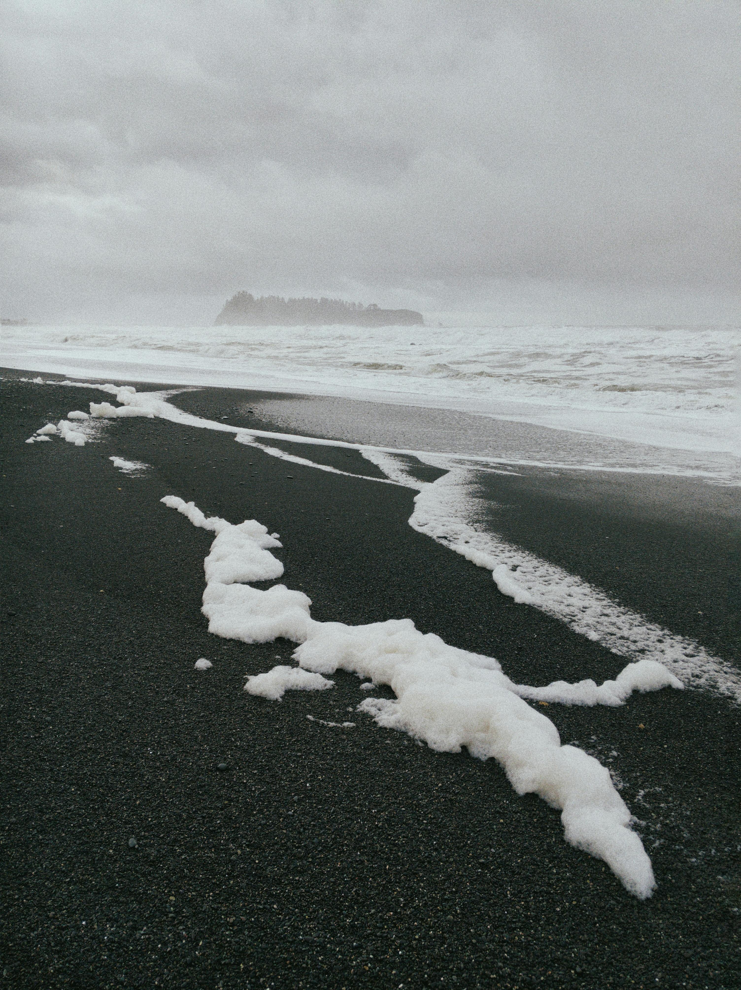 Dramatic view of Oregon coastline with sea foam and overcast skies, capturing nature's rugged beauty.