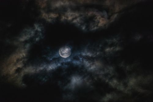 Free A mysterious full moon surrounded by dark clouds, creating an enigmatic night sky scene. Stock Photo