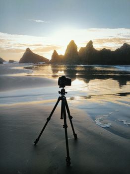 Camera on tripod capturing a serene sunset at a rocky beach shore.