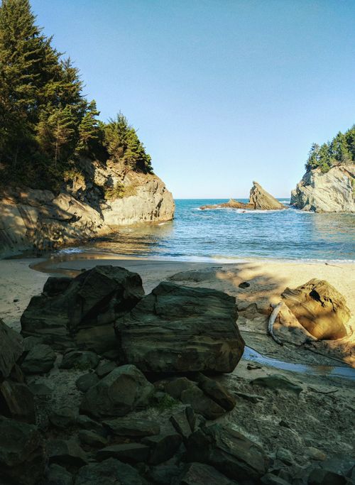 Free Peaceful beach cove with rocky formations and dense forest trees under clear sky. Stock Photo