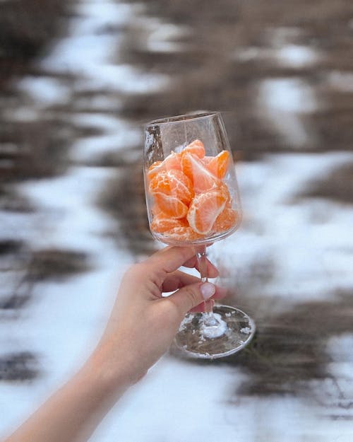 Crop woman with glass of tangerines in snowy forest