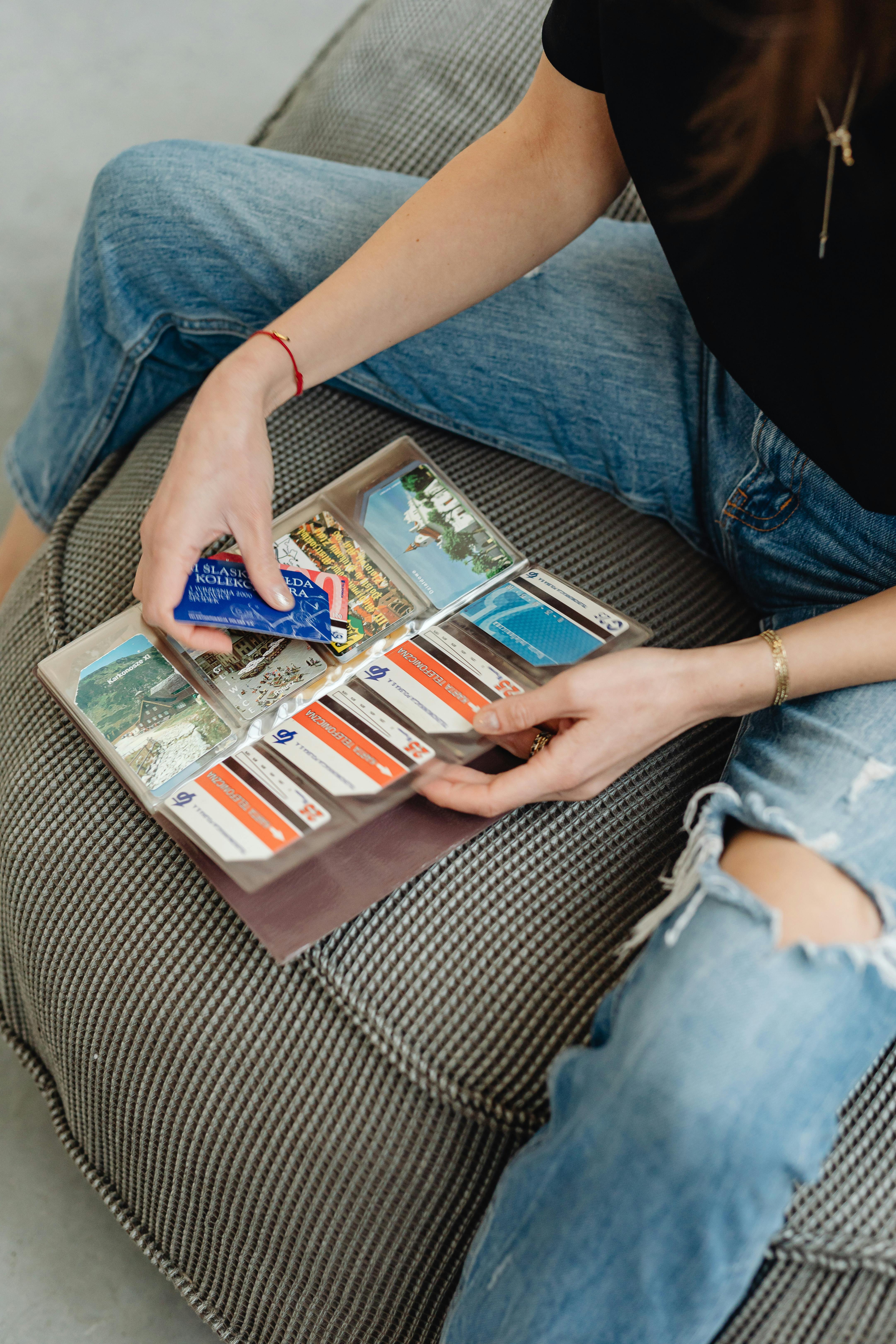 A person flipping through a vintage travel postcard album while seated on a comfortable couch.