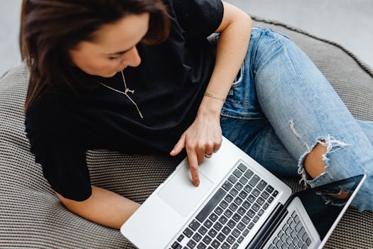 Casual young woman browsing on laptop while relaxing on a cushioned seat.