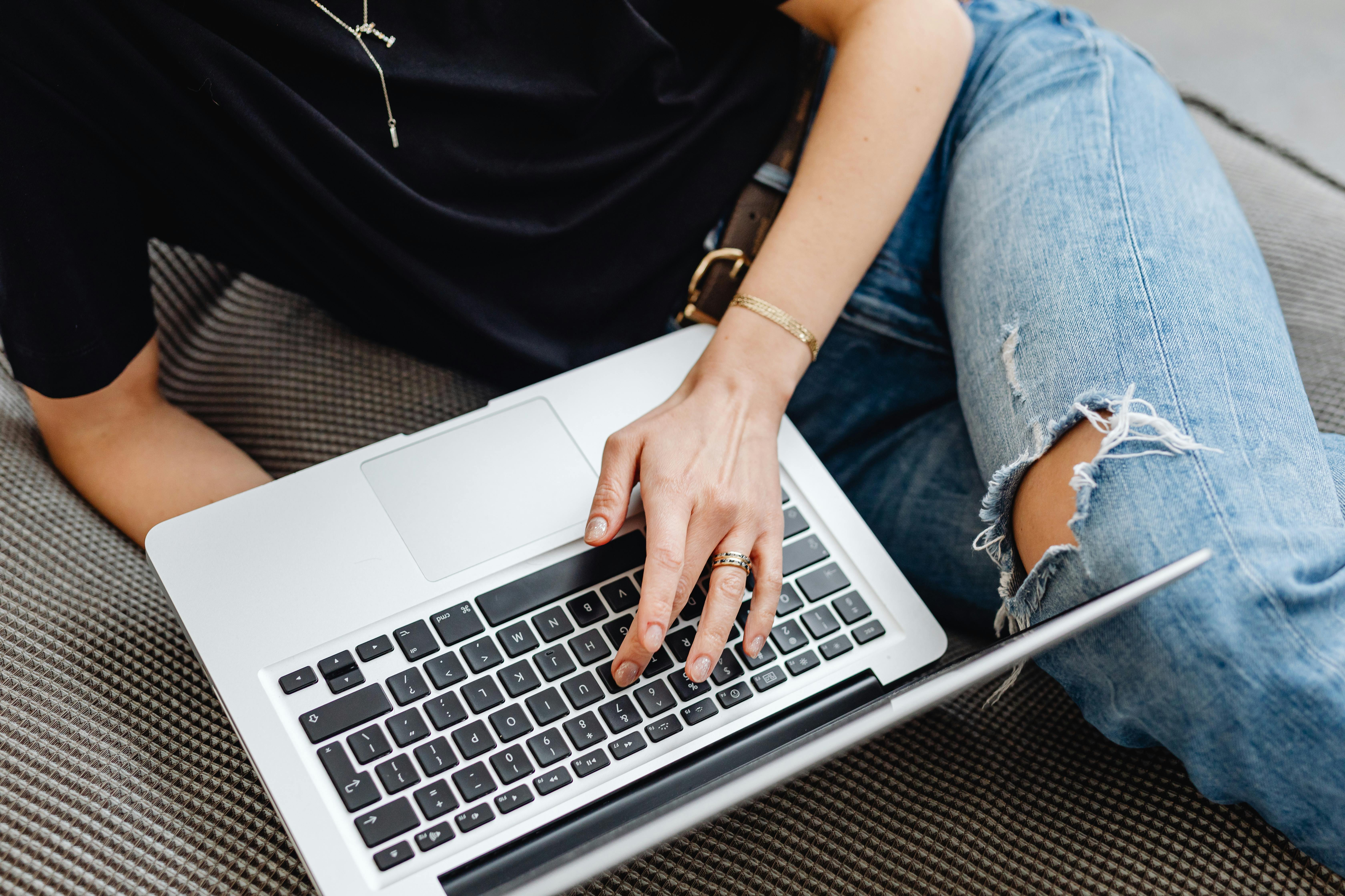 A young adult typing on a laptop while sitting comfortably on a sofa indoors.