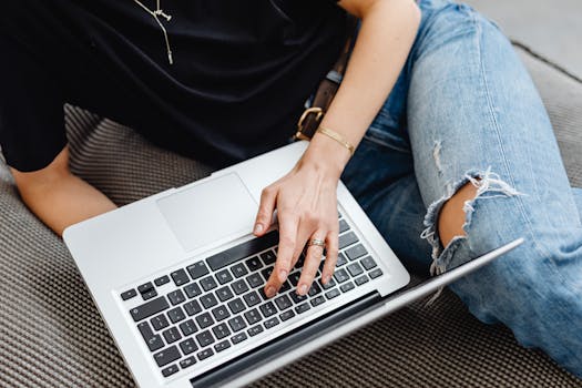 A young adult typing on a laptop while sitting comfortably on a sofa indoors.