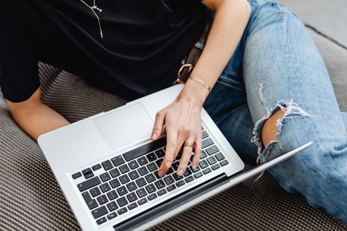 Free A young adult typing on a laptop while sitting comfortably on a sofa indoors. Stock Photo