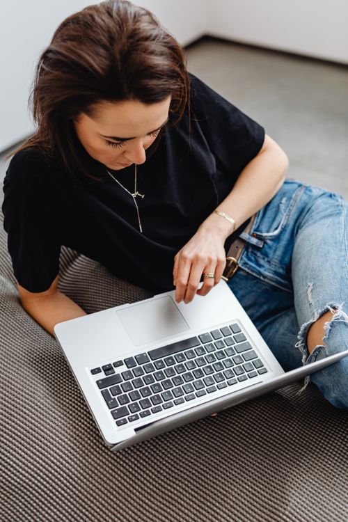Free A young woman in casual clothes uses her laptop while sitting on the floor indoors. Stock Photo