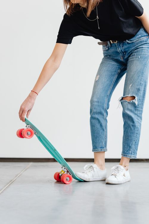 Free Stylish woman in ripped jeans holding a skateboard indoors. Casual and trendy fashion. Stock Photo