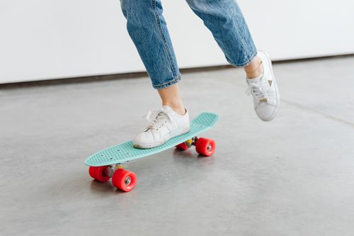 Free Young person riding a colorful skateboard wearing denim jeans and sneakers indoors. Stock Photo