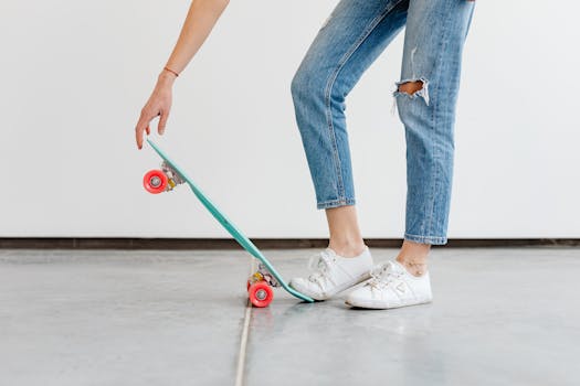 Person in denim jeans and sneakers with skateboard, relaxed indoor setting.