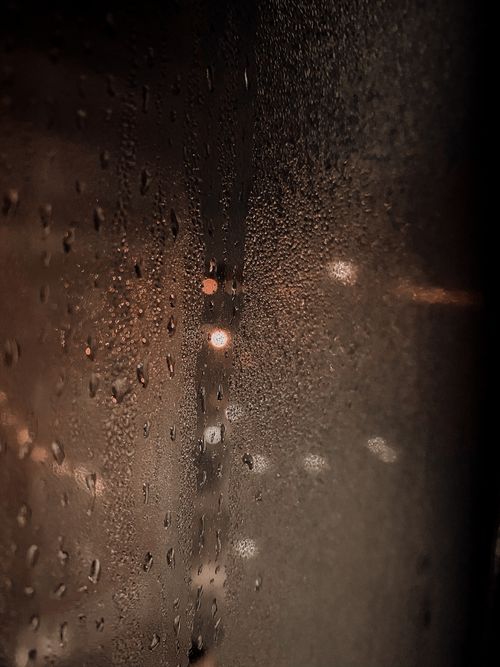Free Abstract blur of street lights of city under dark sky reflecting through wet glass of window with droplets of rain in foggy weather at night Stock Photo