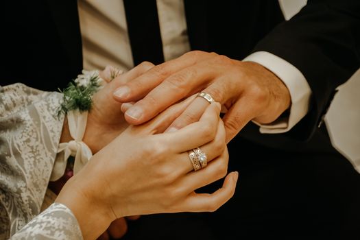 Crop anonymous bride wearing elegant white dress and jewelry golden diamond ring putting on ring on finger of groom on wedding ceremony