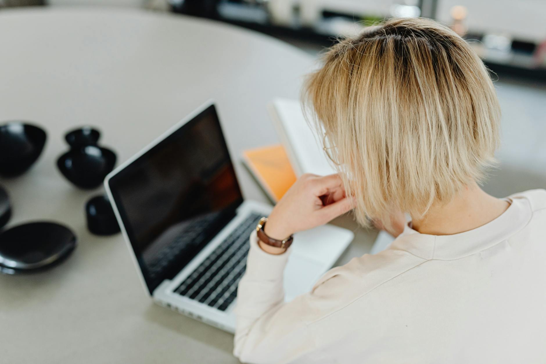 A woman with short blond hair working on a laptop at home.