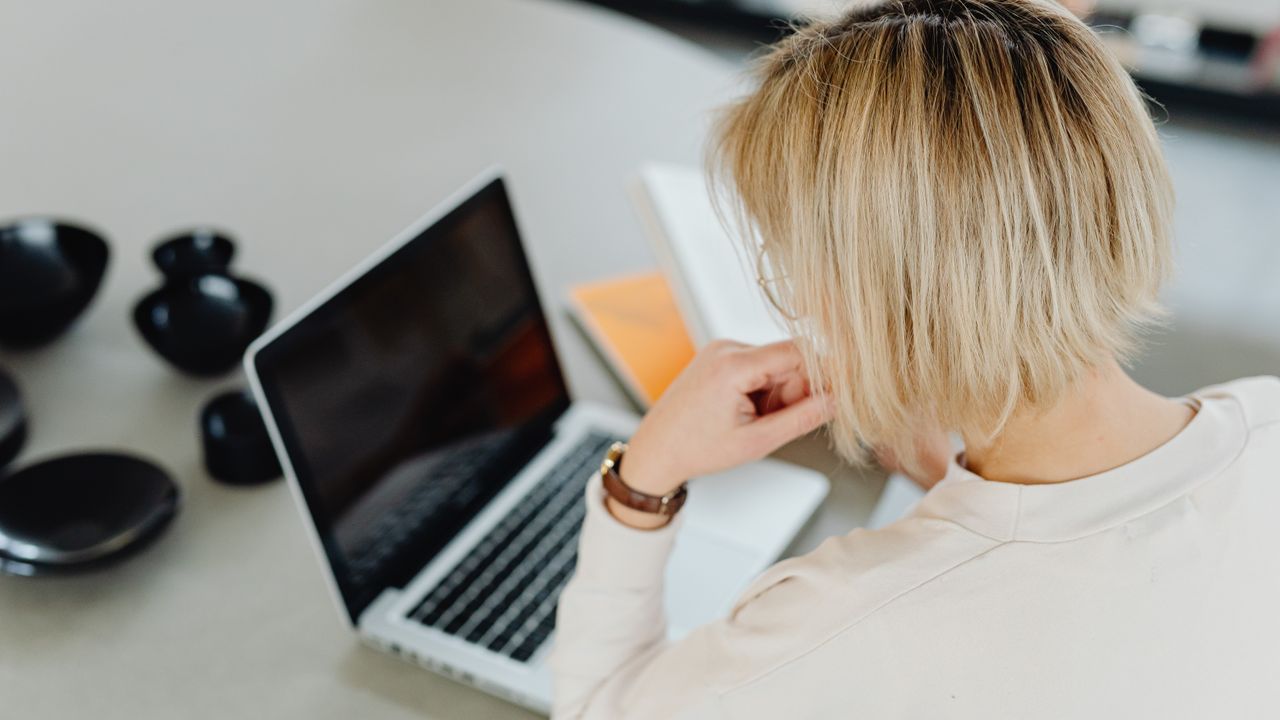 A woman with short blond hair working on a laptop at home.