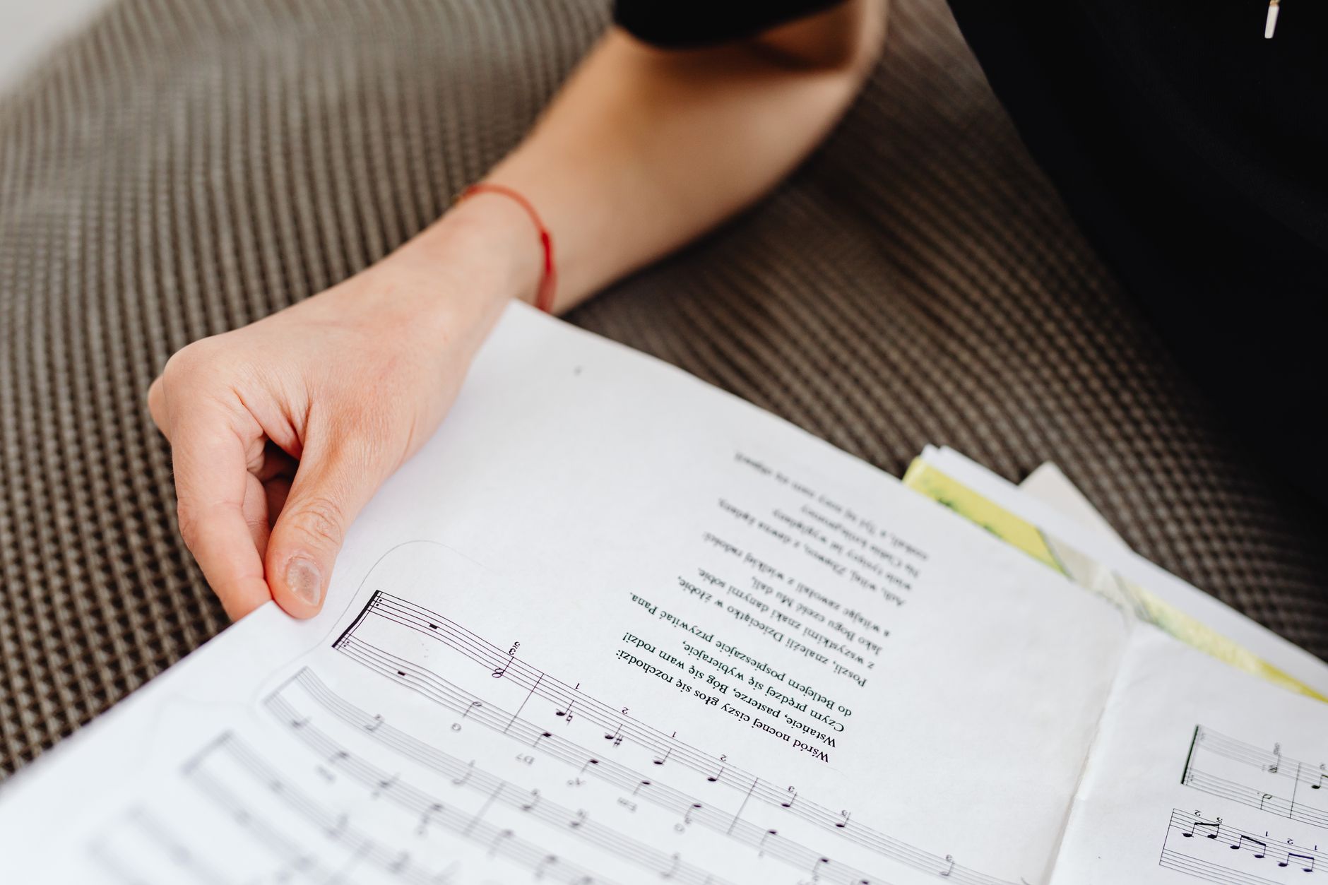Close-up of a hand holding a sheet music on a textured sofa, focusing on musical notes.