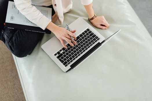 Person working remotely on a laptop with a notebook and pen in hand.