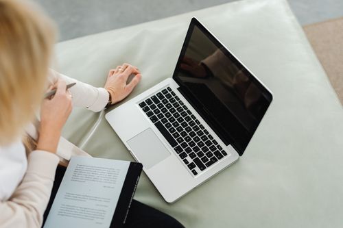 Free A woman using a laptop while taking notes indoors on a comfortable setup. Stock Photo
