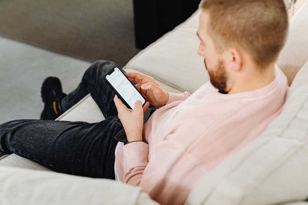 Casual home lifestyle with man using smartphone on couch. Ideal for technology and leisure themes.
