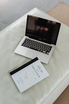 Top view of a laptop and a book on a white couch, offering a minimalist workspace setup.