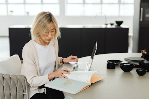 Free A Woman Sitting in Front of a Laptop Reading A Book Stock Photo