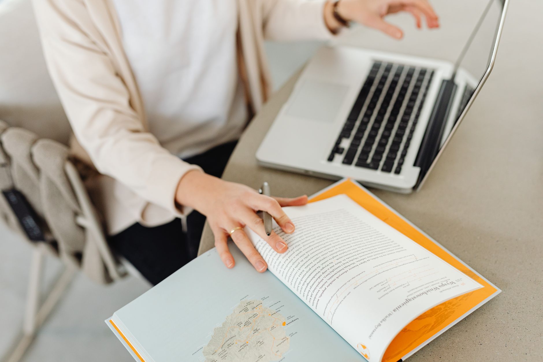 Person working at a desk with an open book, notebook, and laptop, representing organized knowledge work.