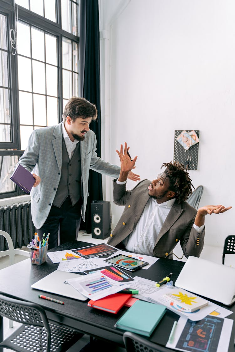 Two Man Disagreeing In An Office And Messy Stationery On A Desk