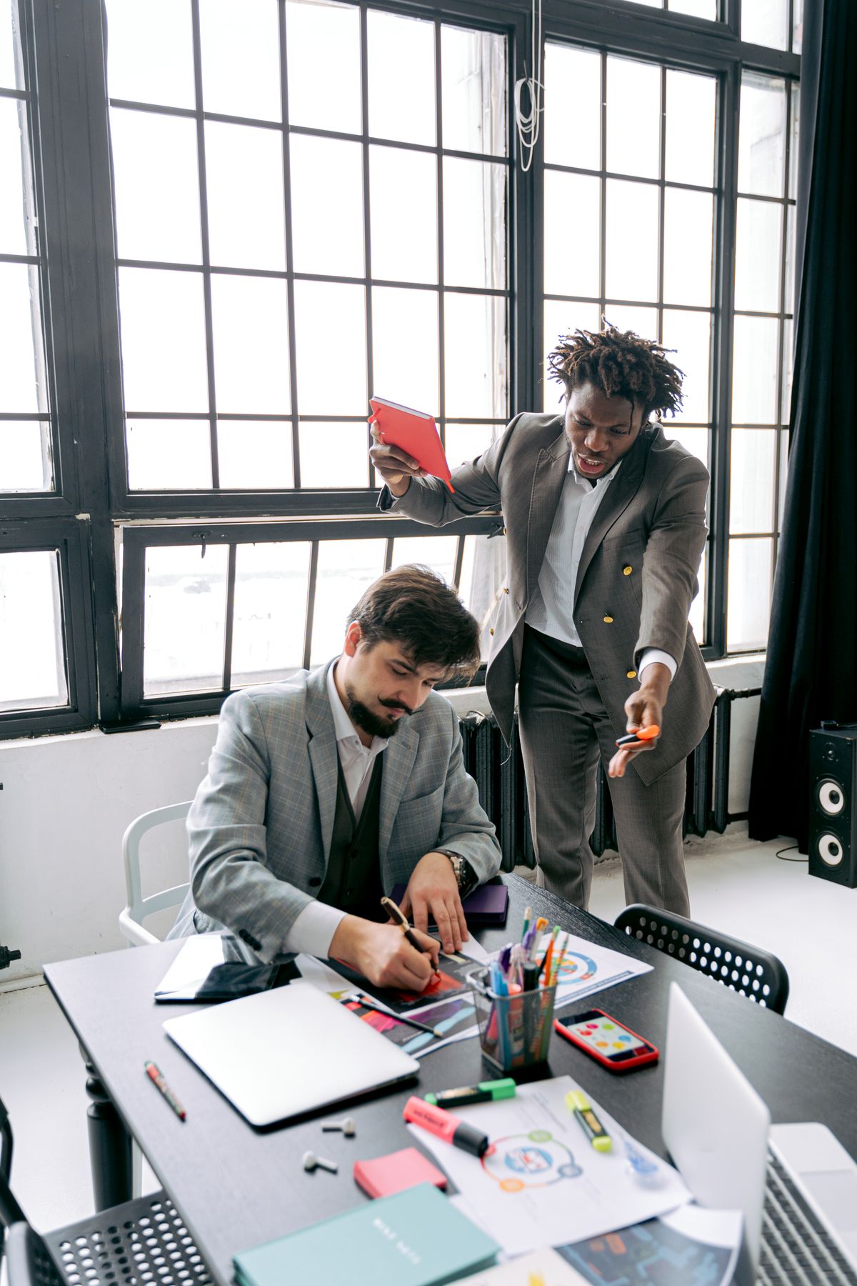 A man leaning over a table gesturing in frustration at two seated colleagues