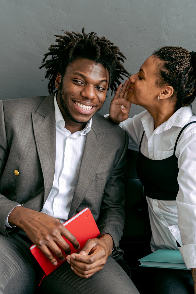 Two professionals sharing a secret on a modern black couch, indoors.