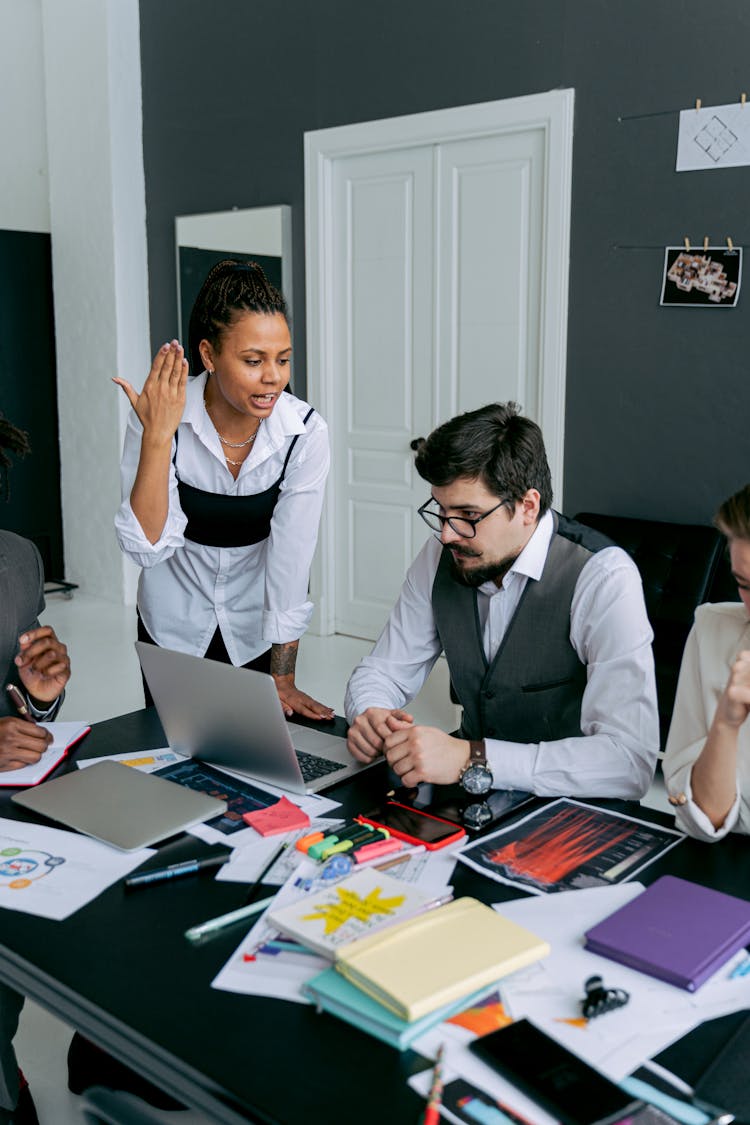 Stationery On A Desk In An Office And Woman Expressing Frustration At A Meeting With Team 