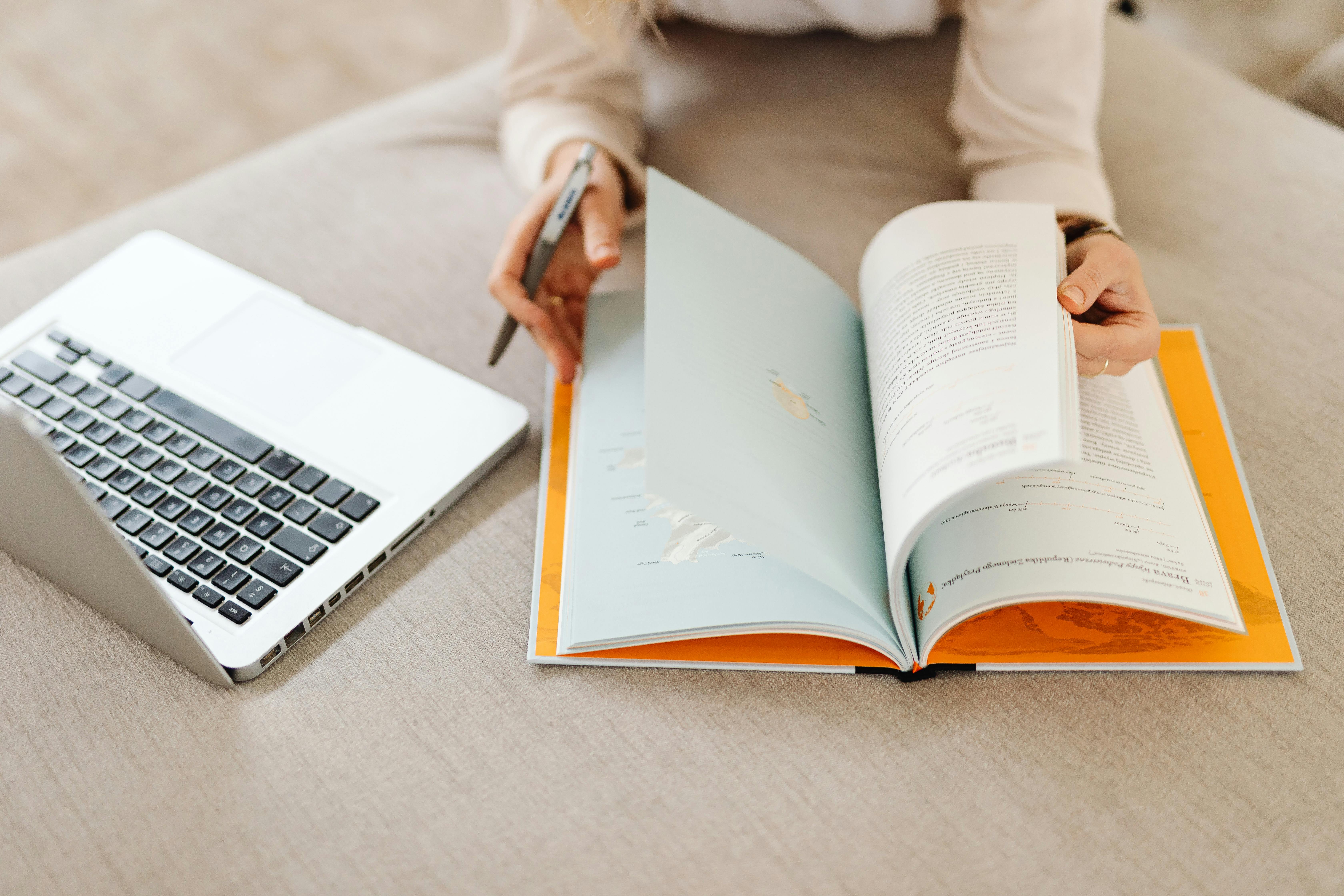 A woman studying comfortably on a sofa with a laptop and book, creating a cozy home atmosphere.