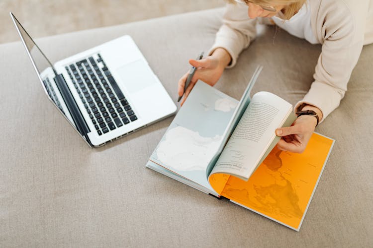 Top View Of A Woman With A Laptop Browsing A Book With Orange Pages On A Matres