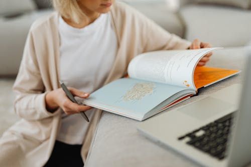 Woman Reading Book and Using Laptop