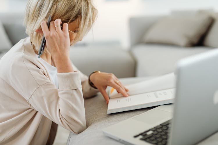 Woman Reading Book And Using Laptop