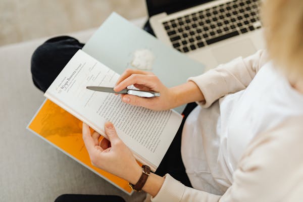 A person reading a book and taking notes for self-improvement