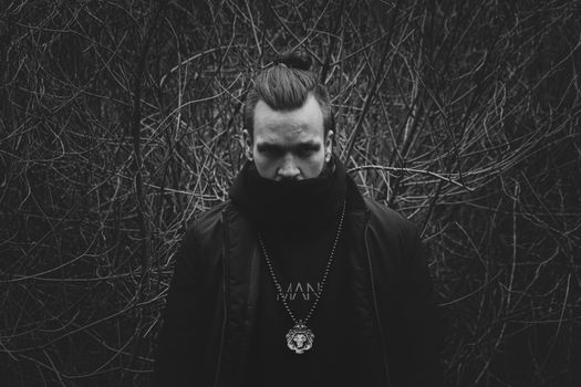 Moody black and white portrait of a man in a scarf standing in a forest.