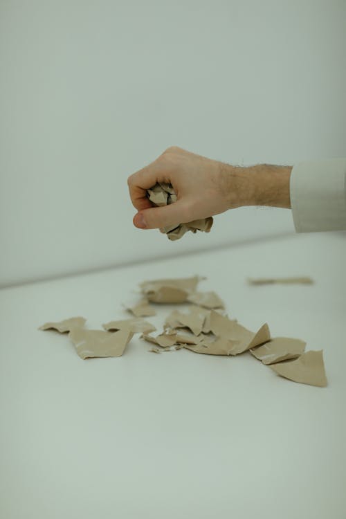 Free Person Holding A Crumpled Paper With Torn Pieces On Table Stock Photo