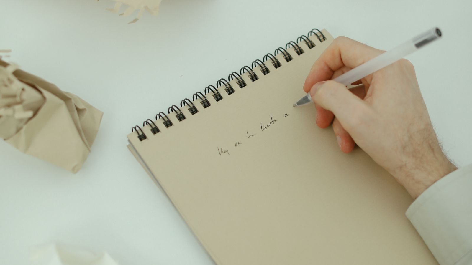 Hands writing on a notepad surrounded by crumpled papers on a table