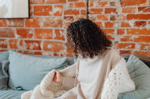 A Woman Wearing Knitted Blanket while Sitting on a Couch