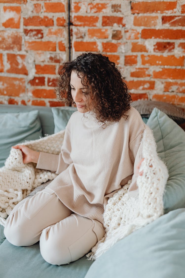 A Woman Wearing Knitted Sweater Relaxing On A Couch While Looking Down