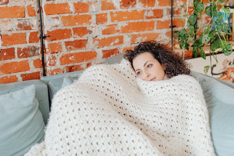 Woman Lying On A Couch Covered With Crochet Blanket While Looking Afar