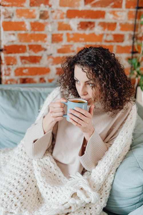 A Woman Sitting on a Couch while Sipping a Hot Tea on a Mug