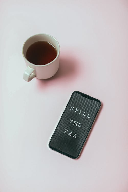 Free A Cellphone Beside a Cup of Tea on a White Surface Stock Photo