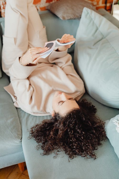 Woman in Sweater Lying on a Couch while Reading a Book
