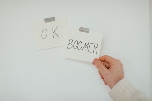 A hand holding a sticky note with the popular phrase 'OK Boomer', illustrating generational dialogue. — photo by Cup of  Couple