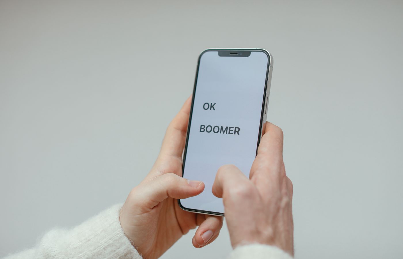 Close-up of a person holding a smartphone displaying 'OK Boomer' against a plain background.