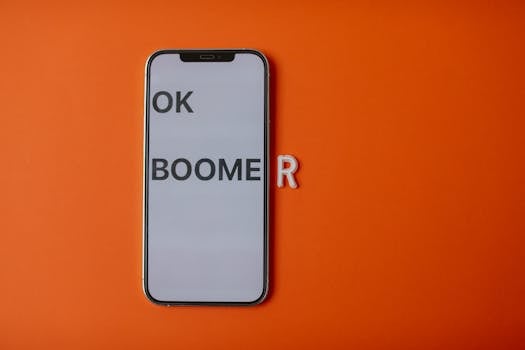 Modern smartphone displaying 'OK Boomer' on orange backdrop, symbolizing generational divide.