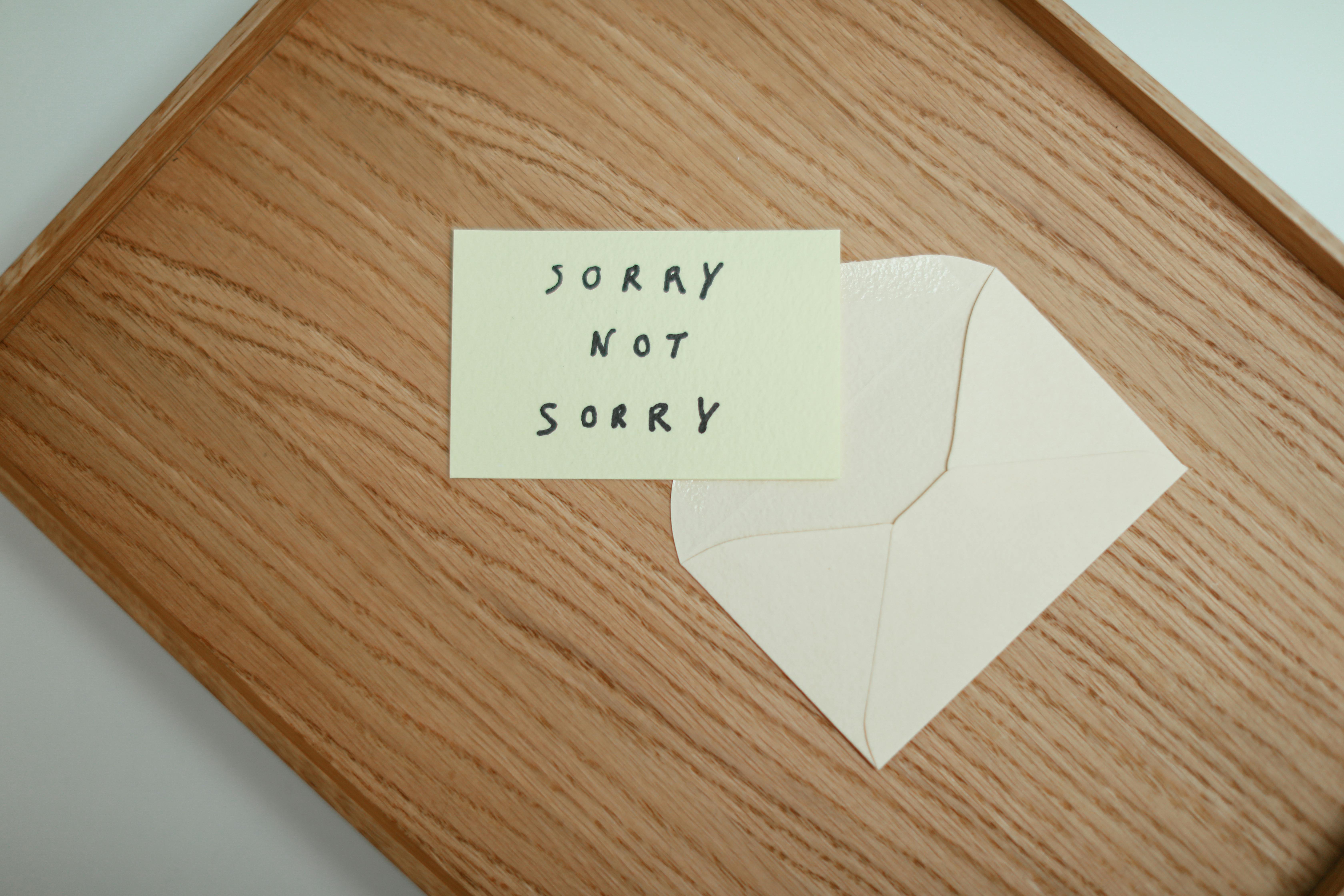 A flat lay of a 'Sorry Not Sorry' card with an envelope on a wooden surface.