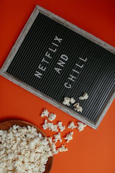 Letter board with 'Netflix and Chill' and popcorn on an orange background, perfect for movie night themes.