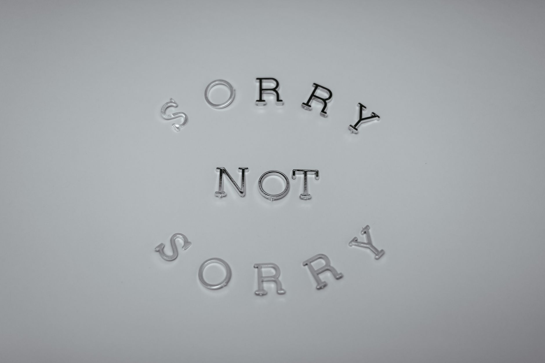 Minimalist design featuring the phrase 'Sorry Not Sorry' arranged in a circular pattern on a white background.